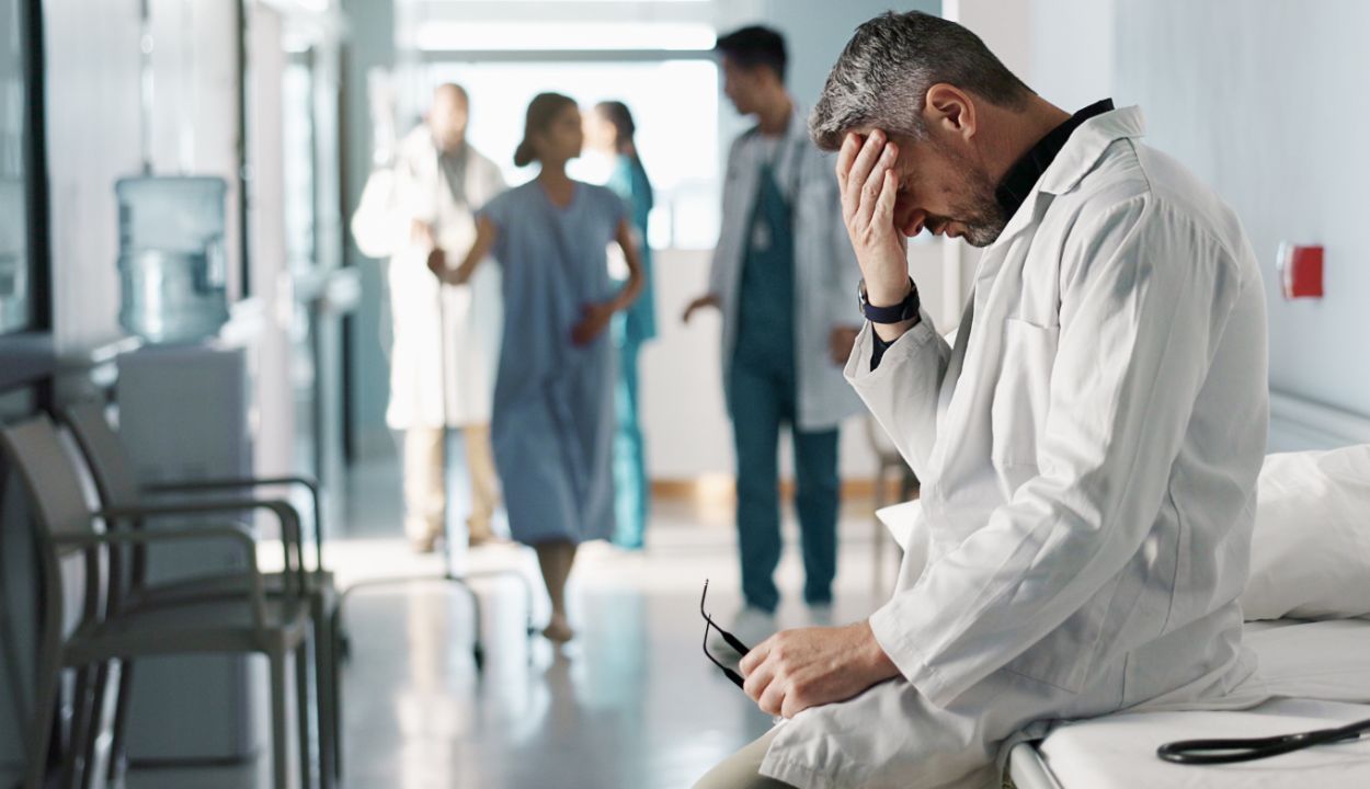 physician in clinic hallway leaning forward with hand over brow