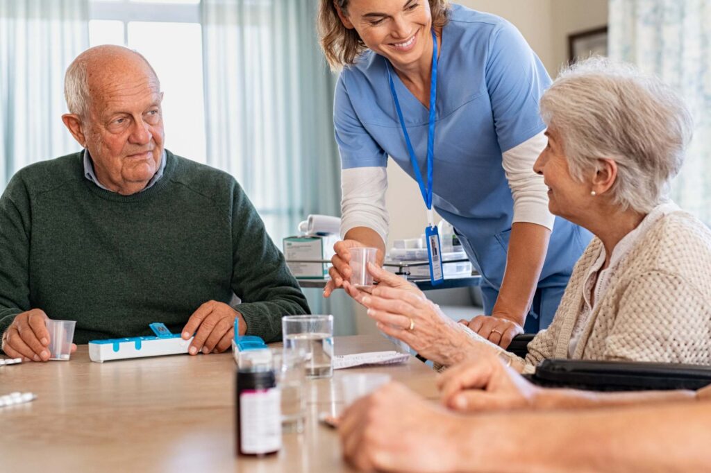 nursing aid assists older couple handing them medications