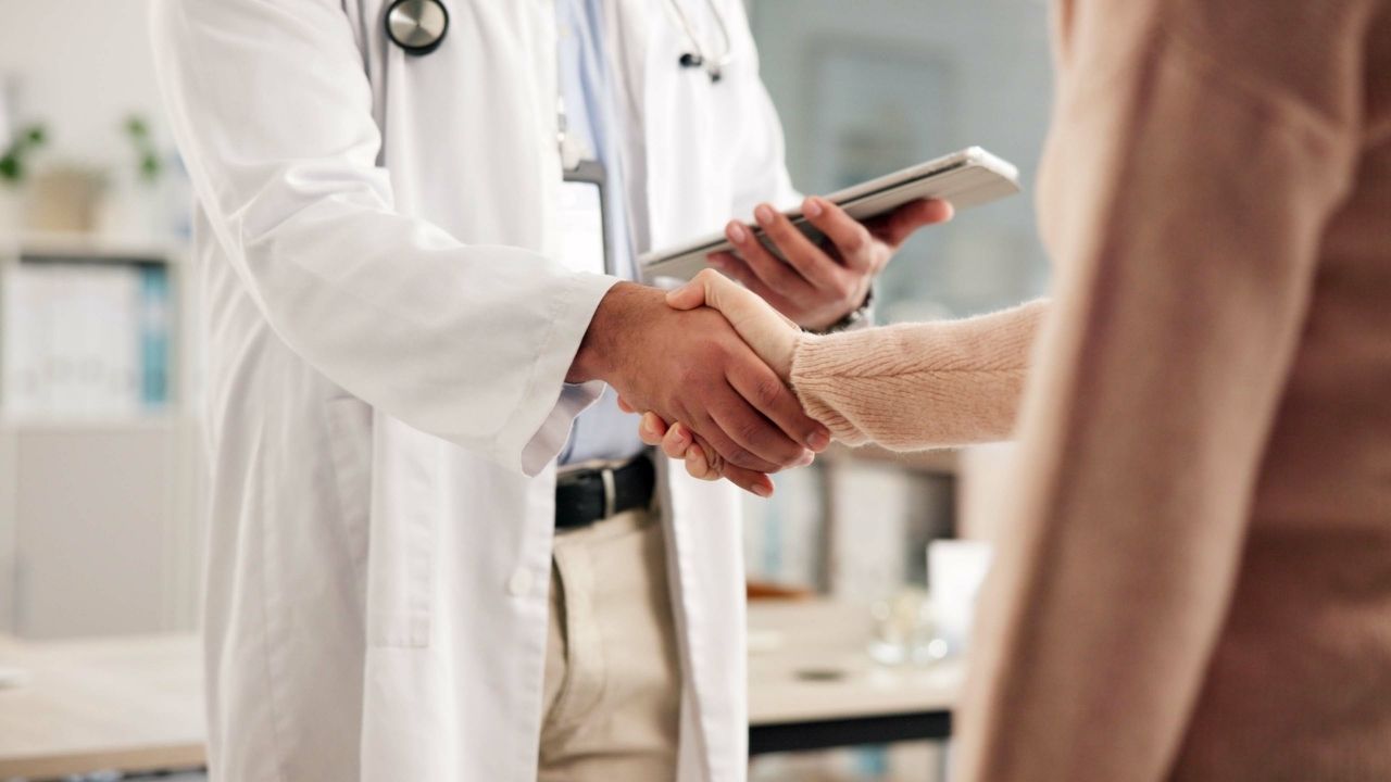 A close-up shot of a doctor in a white lab coat and a patient shaking hands in a bright, modern medical office.