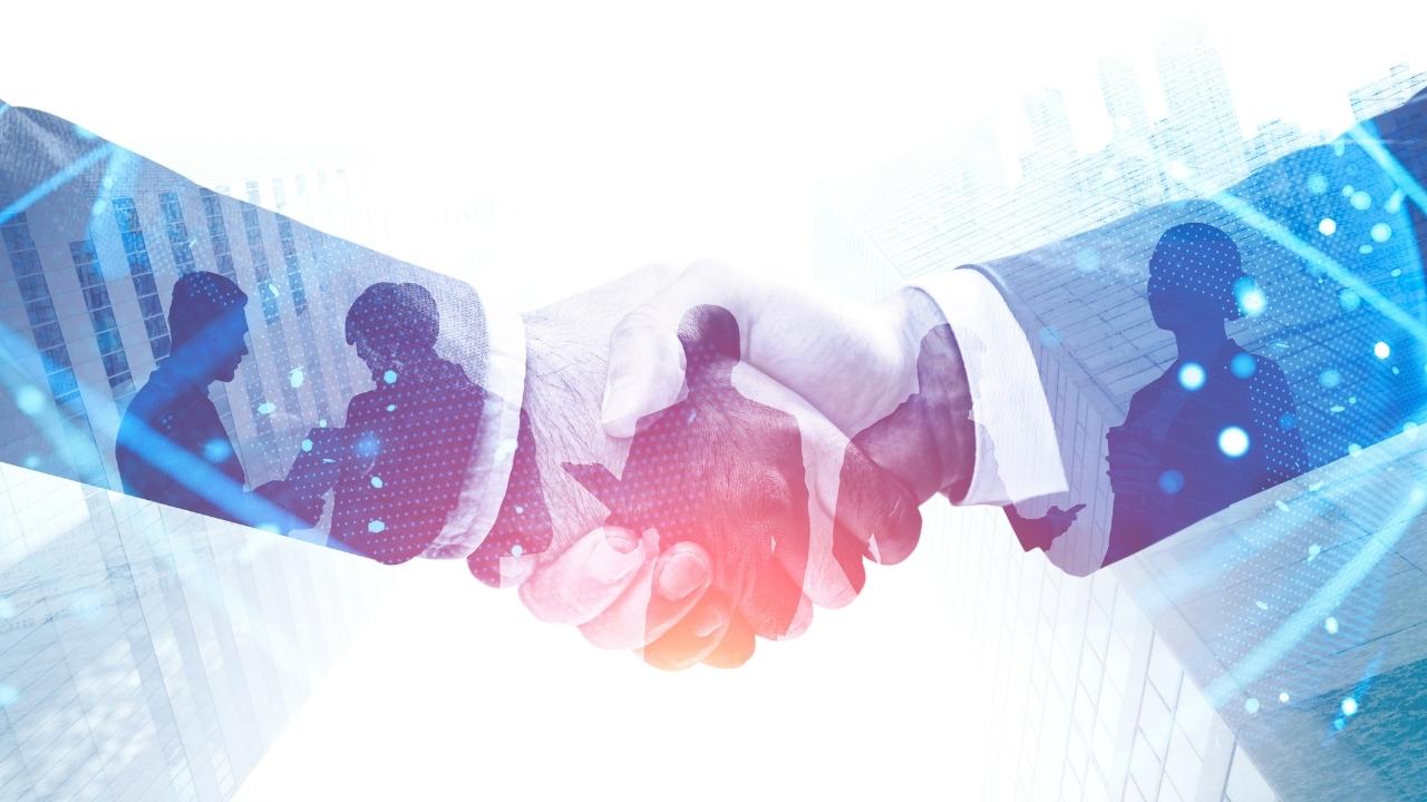 UnisLink & Anatomy Partner for Touchless Healthcare RCM A double-exposure conceptual image of a handshake overlaid with silhouettes of business professionals collaborating and a modern city skyline.